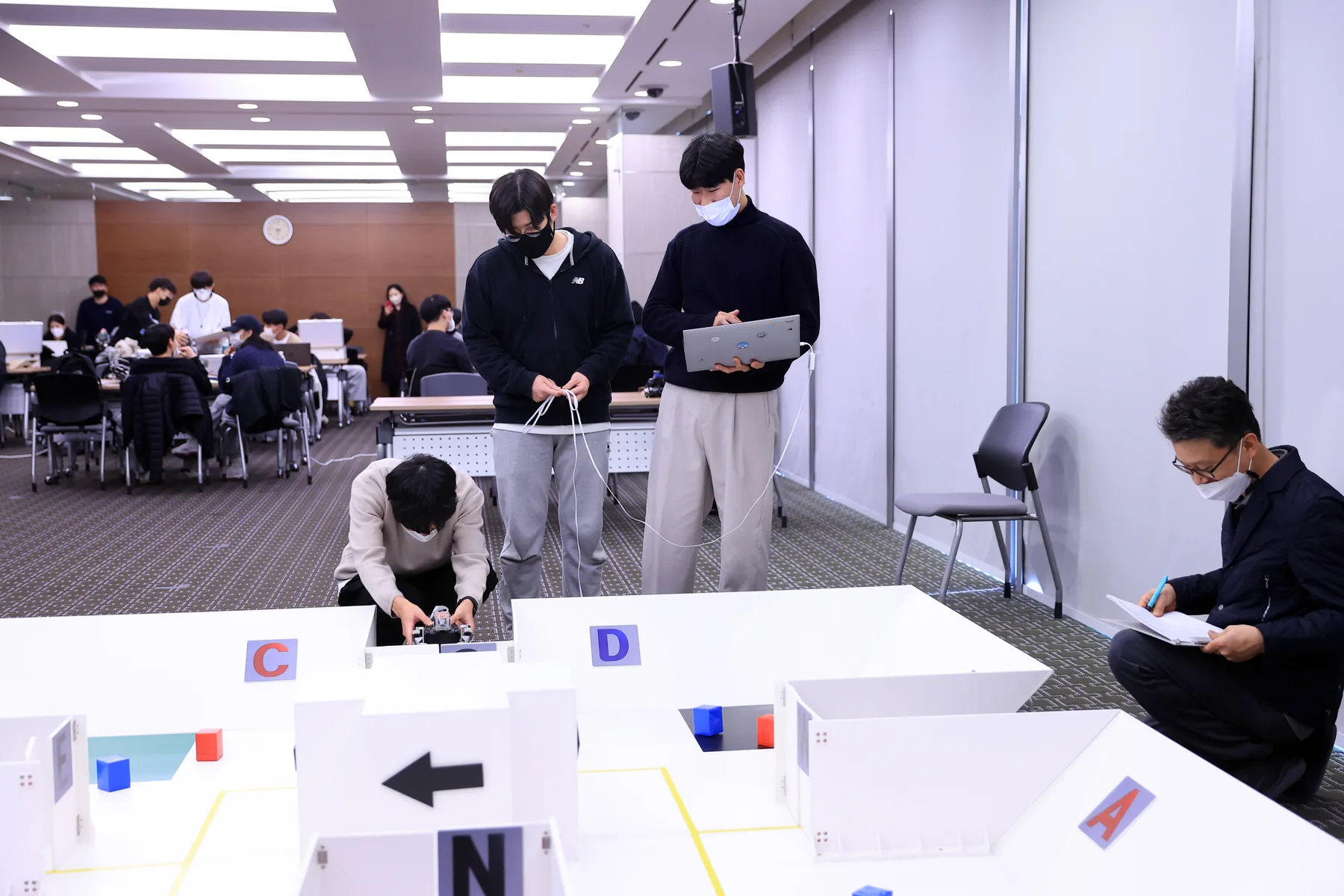 대회장 트랙 앞에서 로봇을 확인하는 팀원들과 뒤쪽 관람석