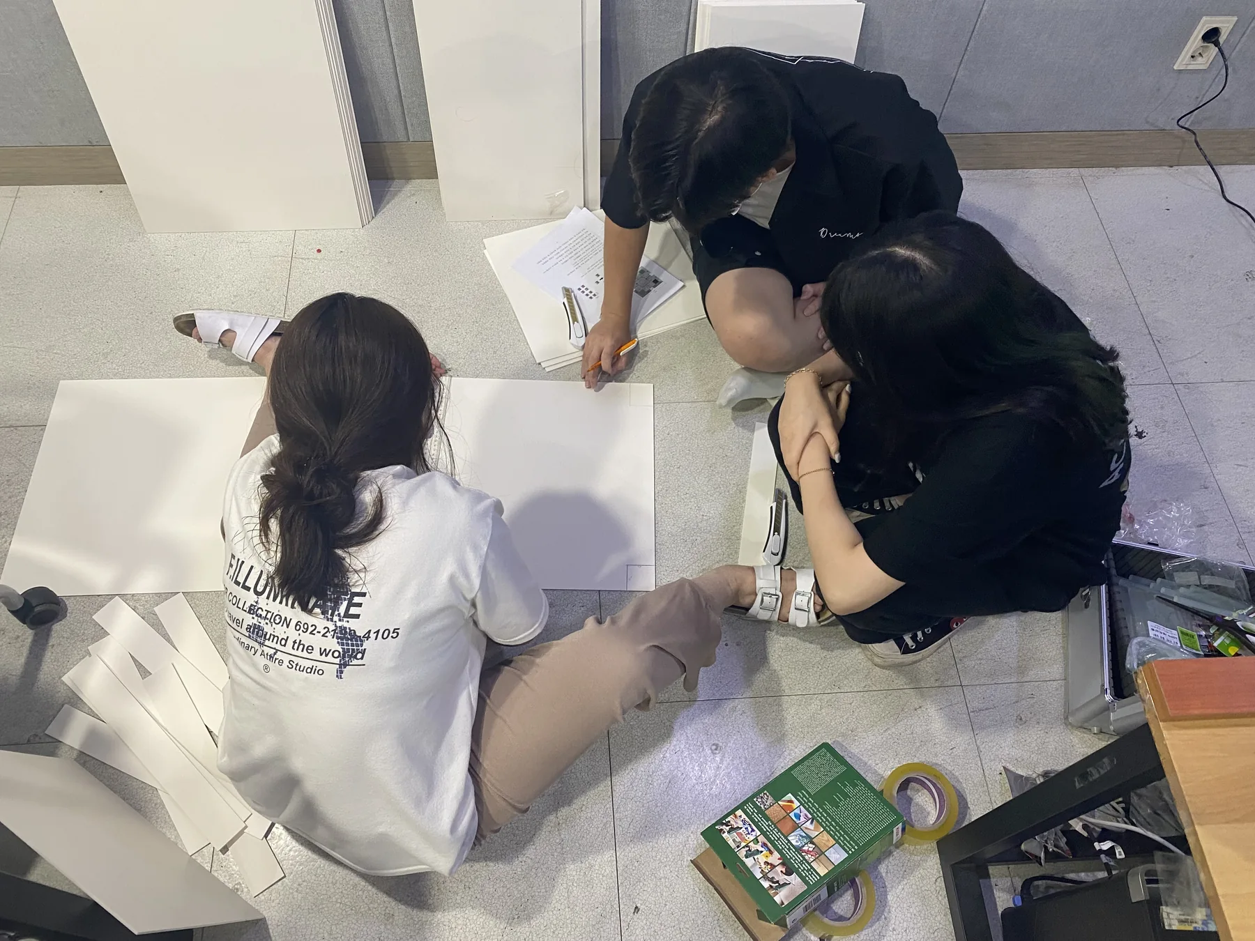 팀원들이 바닥에 종이 구조물을 펼쳐 놓고 로봇 미션 공간을 논의하는 모습